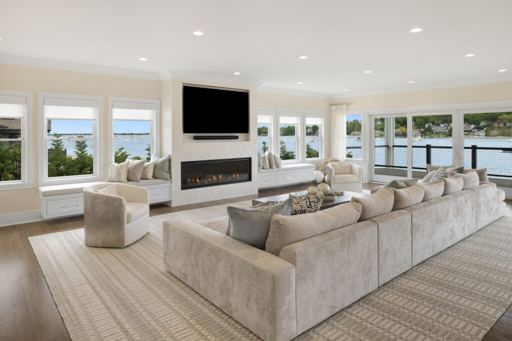 Spacious waterfront living room with panoramic windows, modern fireplace, and plush sectional sofa, showcasing Long Island luxury interior design and turnkey home transformation.